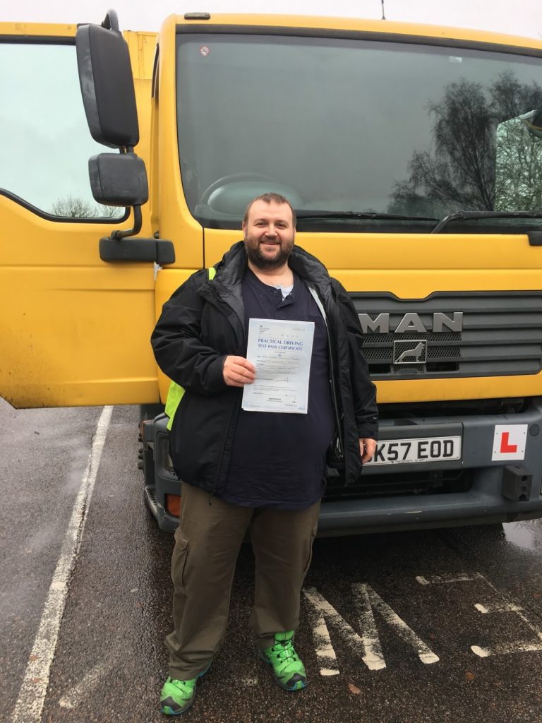 George standing in front of the HGV he trained in, holding his driving test pass certificate